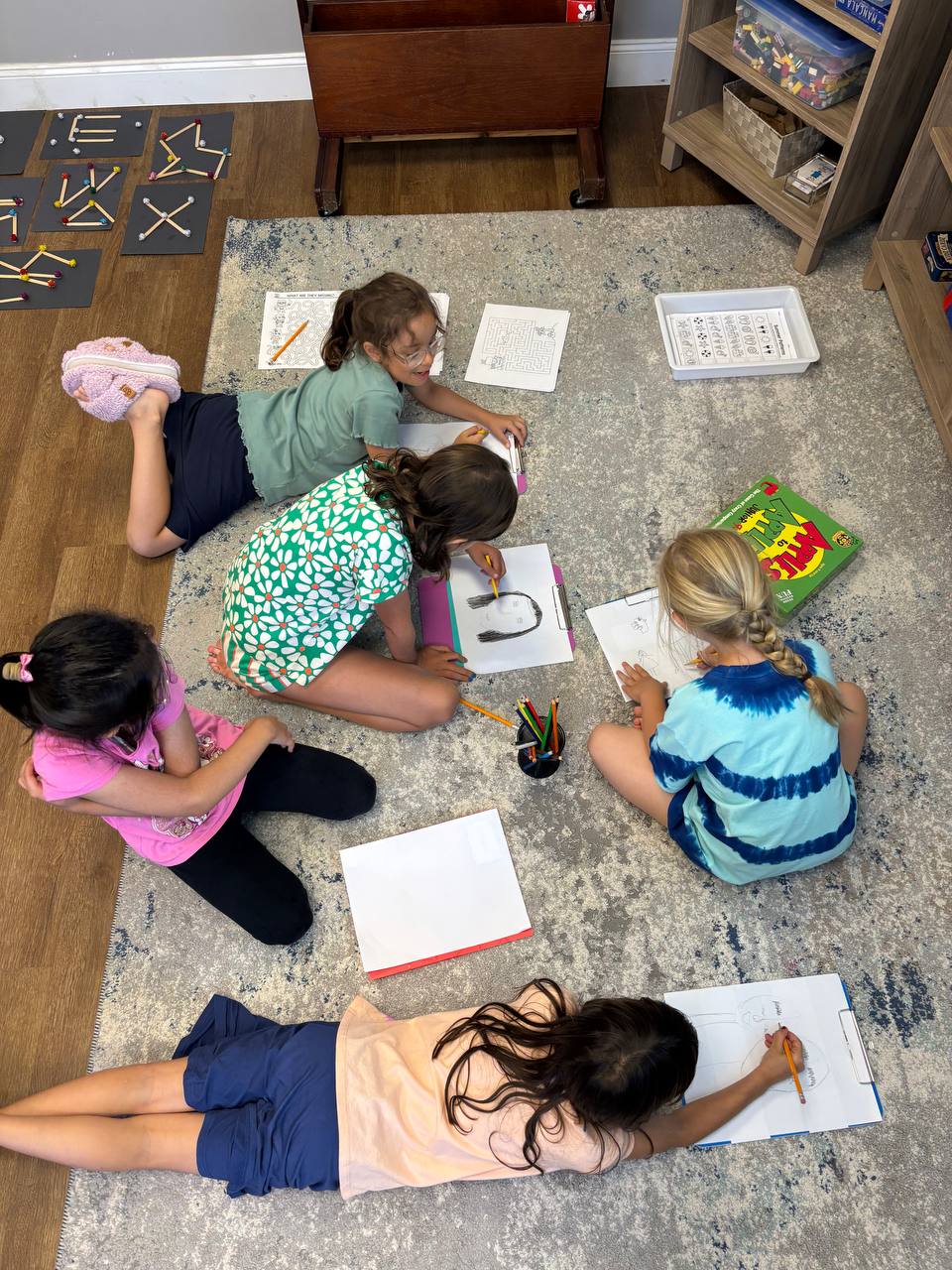 Children lying on a rug drawing and working together at Elements Workspace.