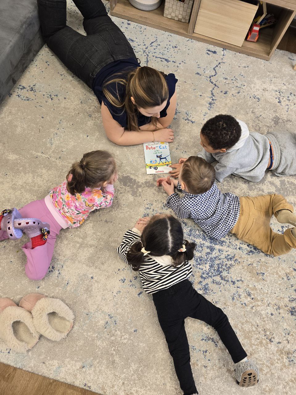 A learning guide reading Pete the Cat to a small group of Starbirds-age children on the rug at Elements Workspace.